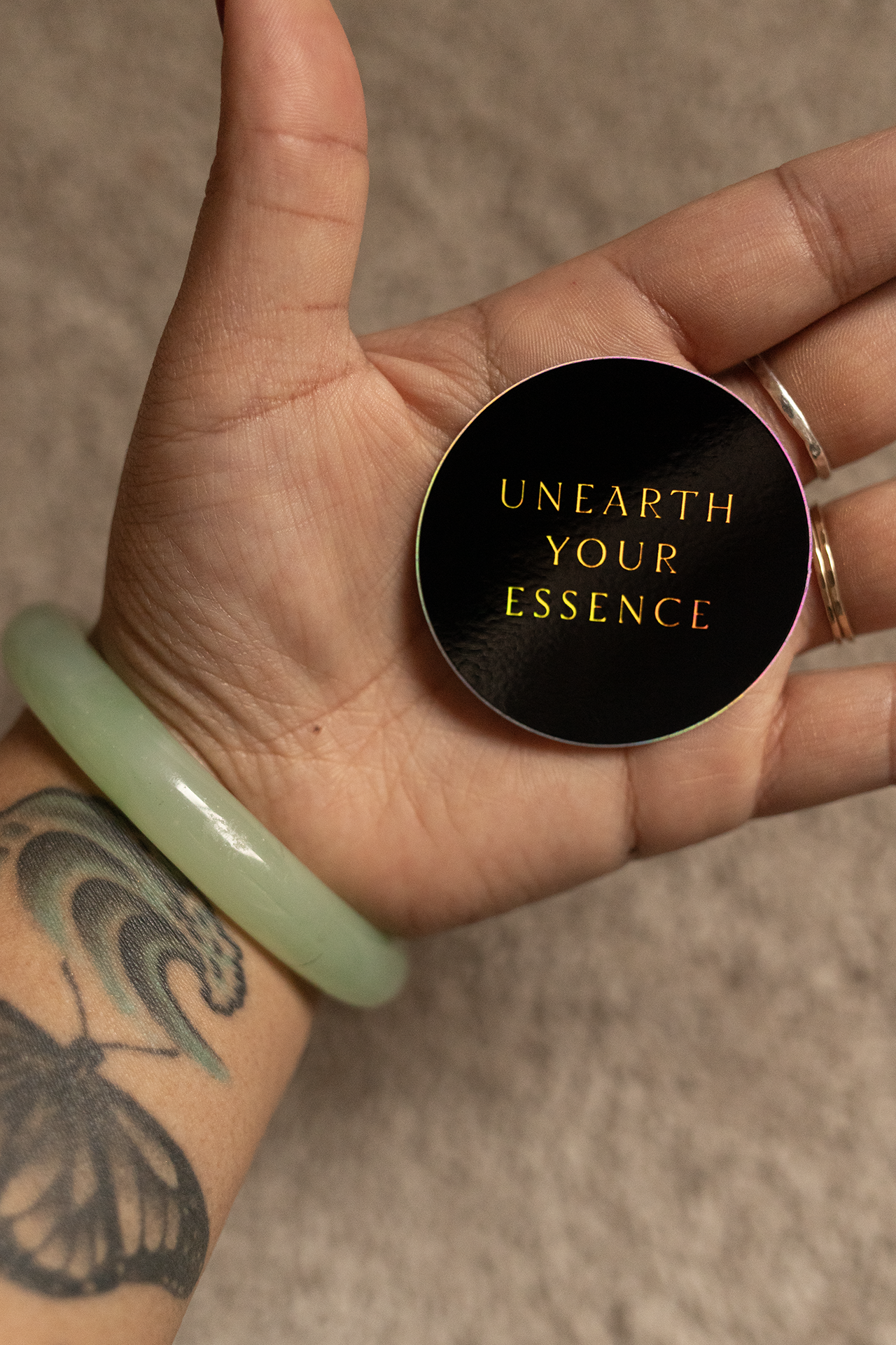 Hand holding round sticker, wearing a jade bracelet