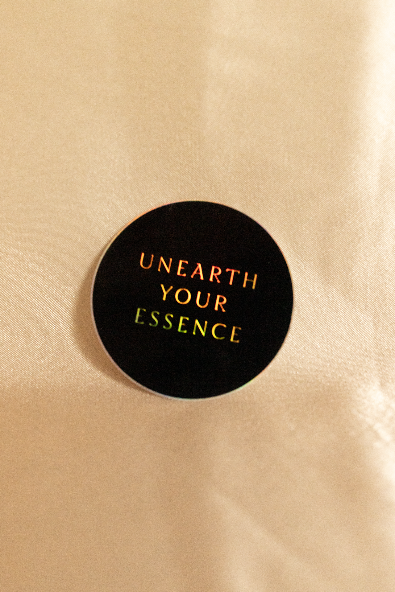 Black circular sticker with 'Unearth Your Essence' text on a beige background